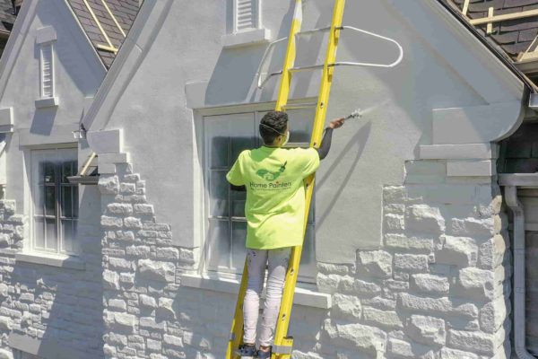 Professional house painter painting exterior of house using ladder and spray, Painter painting exterior brick of house