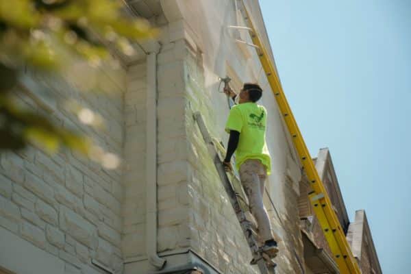 Exterior Painting Brick Painting Light Grey Side View of Male Painter Painting Stone House