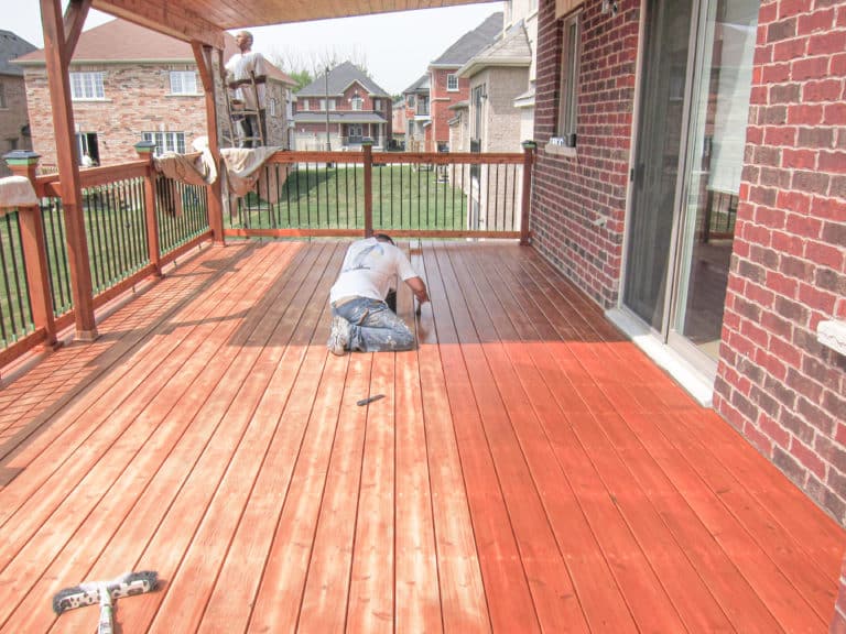 Painter staining large deck with orange stain